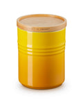 Yellow ceramic jar with wooden lid on a white background, featuring Le Creuset branding.