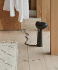 Black handheld steamer on a wooden floor with a mirror reflecting the room.